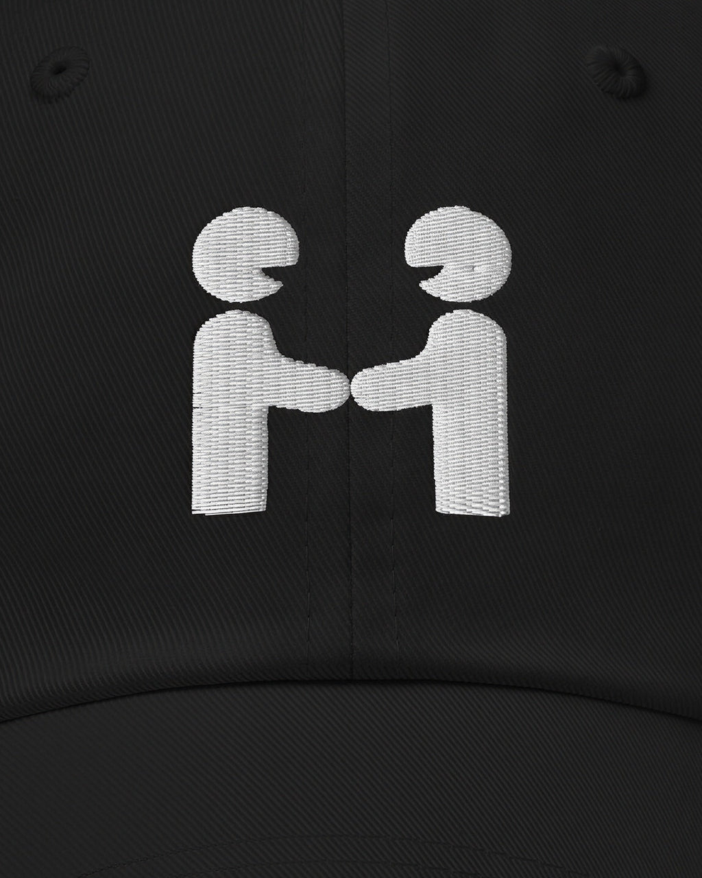 Close-up of the Human-H embroidery on the black cap: two figures shaking hands stitched in off-white thread